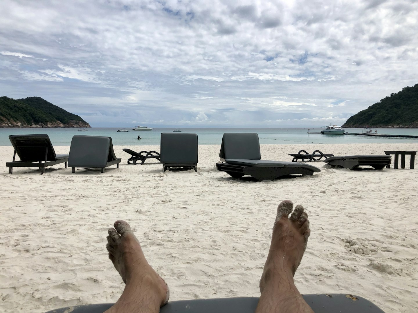 feet on a sunbet with a view of the ovean and white sand, cloudy